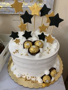 a white cake with gold stars and chocolate candies on top, sitting on a table