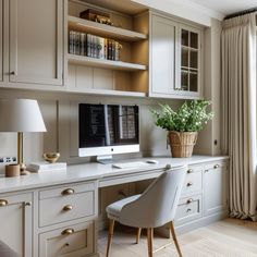 a desk with a computer on top of it next to a lamp and some drawers