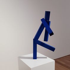 a blue sculpture sitting on top of a white pedestal next to a wooden floor and wall