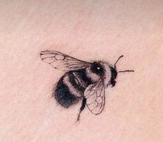 a small tattoo of a bee on the back of a woman's left shoulder