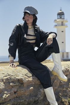 a woman sitting on top of a rock next to a lighthouse