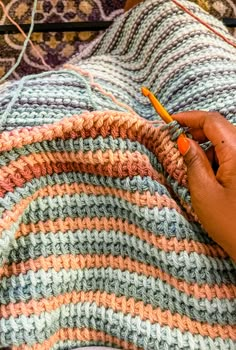 a person is knitting on a blanket with an orange crochet hook in their hand