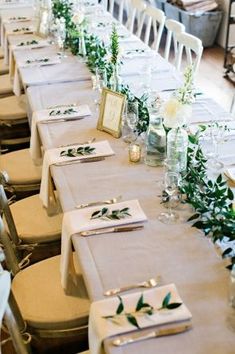 a long table is set up with place settings and greenery on the runneres