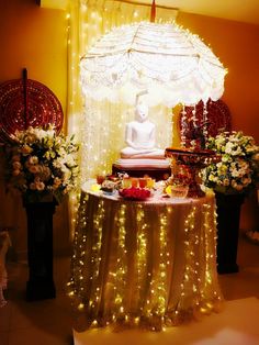 a buddha statue sitting on top of a table covered in flowers and lights next to a window