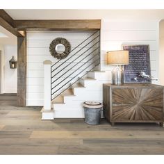 a room with white walls and wood floors, a wooden staircase and a round mirror on the wall