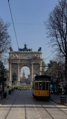 a yellow trolley is on the tracks in front of an arch