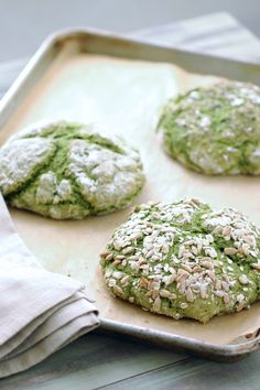 four cookies with green toppings on a baking sheet covered in powdered sugar and sprinkled with sesame seeds