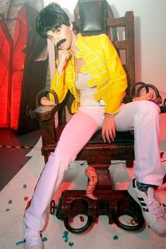 a man sitting on top of a wooden chair in front of a wall covered with confetti