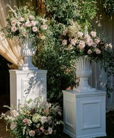 two tall white vases with flowers in them sitting on the ground next to each other