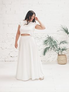 a woman standing in front of a brick wall wearing a white skirt and crop top