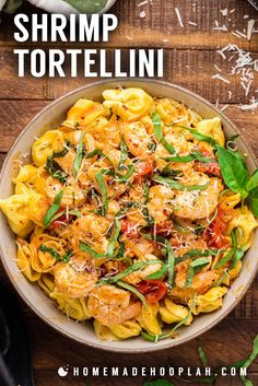 shrimp tortelli with spinach and tomatoes in a white bowl on top of a wooden table