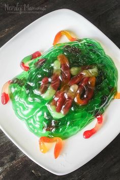 a white plate topped with vegetables covered in green sauce and gummy bears on top of it