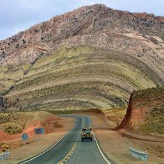 a truck is driving down the road in front of a large mountain with hills on both sides