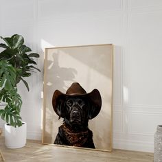 a black dog wearing a cowboy hat sitting in front of a framed photograph on a wooden table