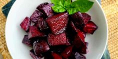 a white bowl filled with sliced beets on top of a green leafy table