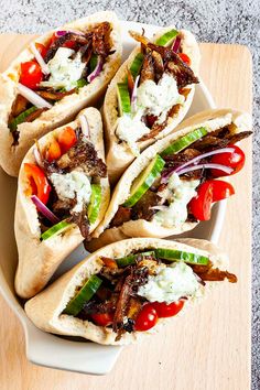 four pita breads with meat, vegetables and sauce on a white plate next to a wooden cutting board