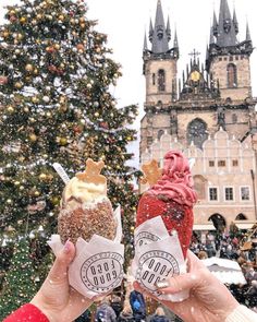 two people holding up their ice cream cones in front of a christmas tree and castle