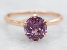 an oval shaped pink sapphire ring in yellow gold, set on a plain surface with a thin band