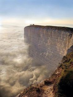 two people standing on top of a cliff above the clouds in the sky with their backs to the camera