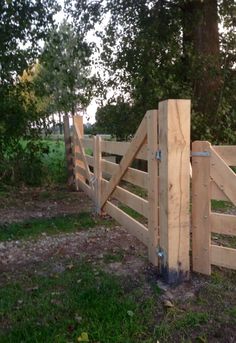 a wooden fence in the middle of a grassy area with trees and grass around it