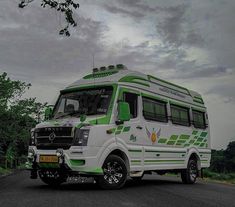 a green and white bus is parked on the side of the road in front of some trees