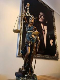 a statue of lady justice holding the scales of justice in front of a framed portrait