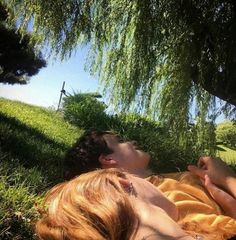 two people laying in the grass under a tree