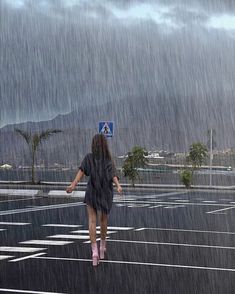 a woman walking across a parking lot in the rain