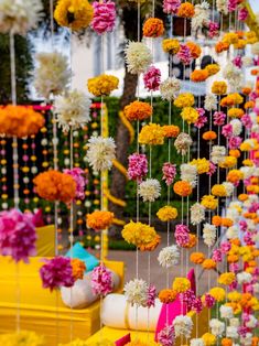 an arrangement of flowers hanging from strings in front of a yellow table with pink and white chairs