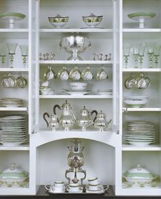 a white china cabinet filled with lots of dishes and silver ware on top of it