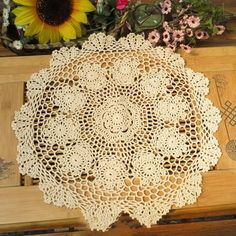 a doily is sitting on top of a wooden table next to flowers and a sunflower