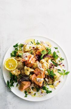 a white plate topped with shrimp, cauliflower and broccoli next to a lemon wedge