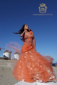 a woman in an orange dress standing on the beach with her hair blowing in the wind