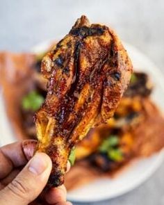 a person holding up a piece of meat on a plate with other food items in the background