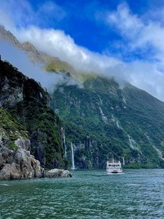 a boat is in the water near a mountain and some clouds are flying over it