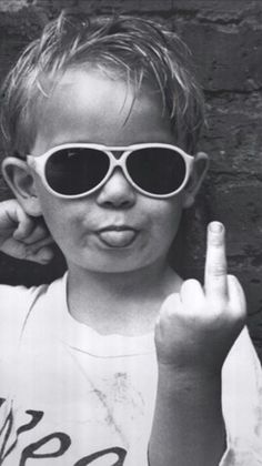 a black and white photo of a young boy wearing sunglasses making the peace sign with his fingers