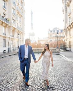 a man and woman holding hands while walking down a cobblestone street in front of the eiffel tower