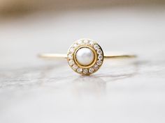 a pearl and diamond ring sitting on top of a white surface with a gold band