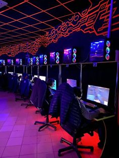 a room filled with lots of computer monitors and gaming equipment in front of neon lights