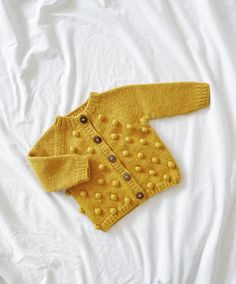 a yellow knitted cardigan laying on top of a white sheet with buttons and holes