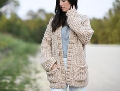 a woman standing on the side of a road wearing a cardigan sweater and jeans