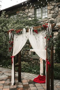 an outdoor wedding ceremony setup with white drapes and red flowers on the arbors