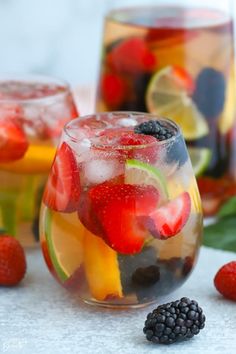 a glass filled with fruit and ice sitting on top of a table next to berries