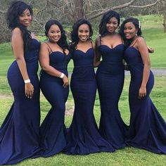 four beautiful women in blue dresses posing for the camera on a grassy field with trees behind them