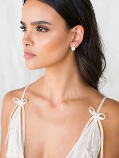 a woman wearing a white dress with bows in her hair and earrings on her neck