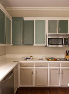 a kitchen with white cabinets and green cupboards on the wall, wood flooring