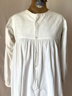 "1815. 32\" bust, white cotton chemise  with long wide sleeves, round neckline, bounle lined yoke, high waisted bodice. Chemise has full skirt to floor and fastens in front, from neck to below knees  with 5 small white glass buttons. Measurements: 32\" bust  Shoulder to shoulder 14\" Shoulder to hem  46\" Ar.holes 7\" Sleeves 20\" Neckline 7\" wide, 3\" deep  Width at bottom 72\" Condition very good,  small rust dots in front" Cotton Victorian Dress With Buttons For Daywear, Victorian Cotton Prairie Dress With Long Sleeves, Victorian Cotton Prairie Dress For Daywear, Long Sleeve Cotton Dresses With Historical Design, Long Sleeve Cotton Dress With Historical Design, Cotton Long Sleeve Dresses With Historical Design, Historical Design Long Sleeve Dress For Daywear, Historical Long Sleeve Dresses For Daywear, Long Sleeve Dresses With Historical Design For Daywear