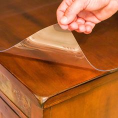 a person holding a piece of clear plastic on top of a wooden table with a drawer