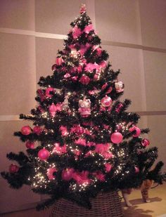 a pink and black christmas tree in a basket with lights on it's sides