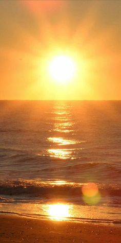 the sun is setting over the ocean with surfers